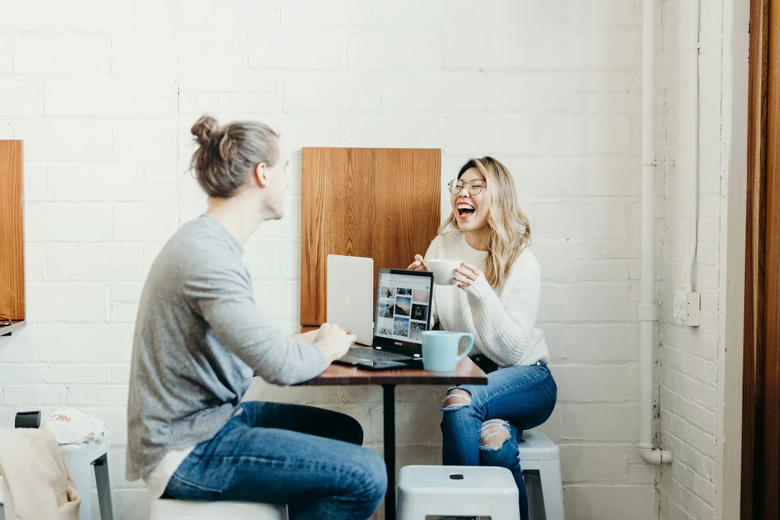 Two people talking across a table with a laptop in a cafe